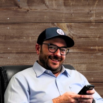 Man in a cap smiling and using a smartphone in an office chair.