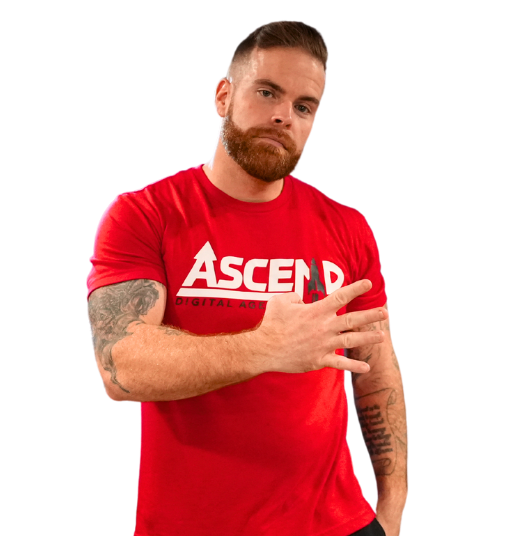 Man in red 'Ascend' shirt with tattoos displaying hand gesture.