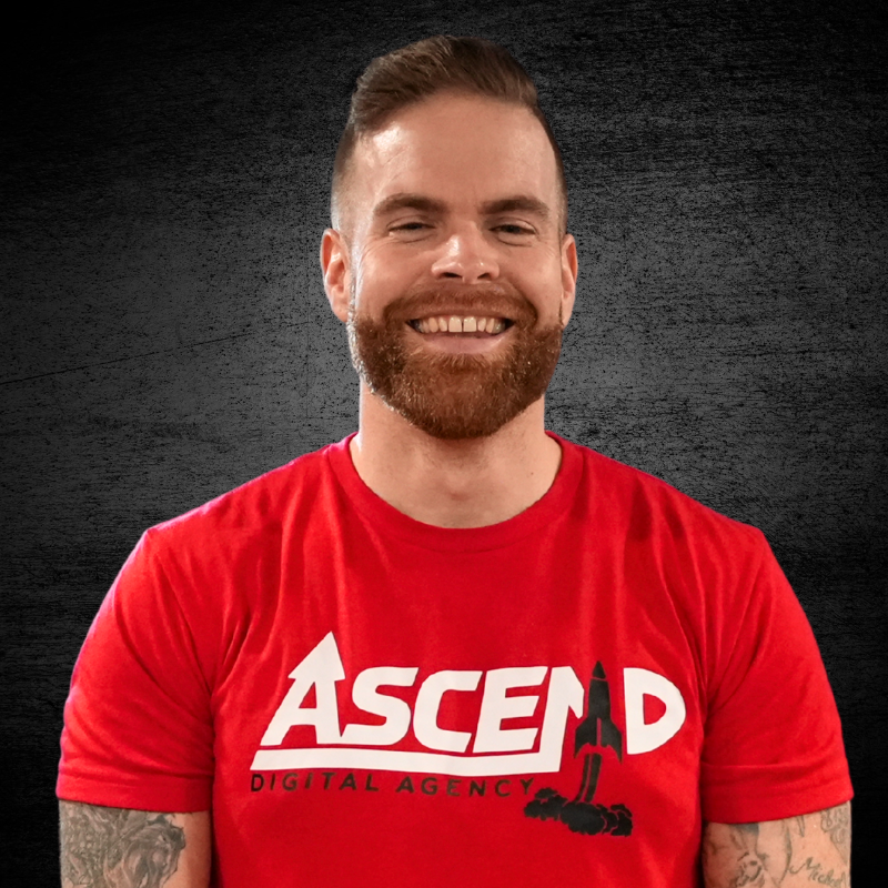 Smiling man in red Ascend Digital Agency t-shirt with dark background