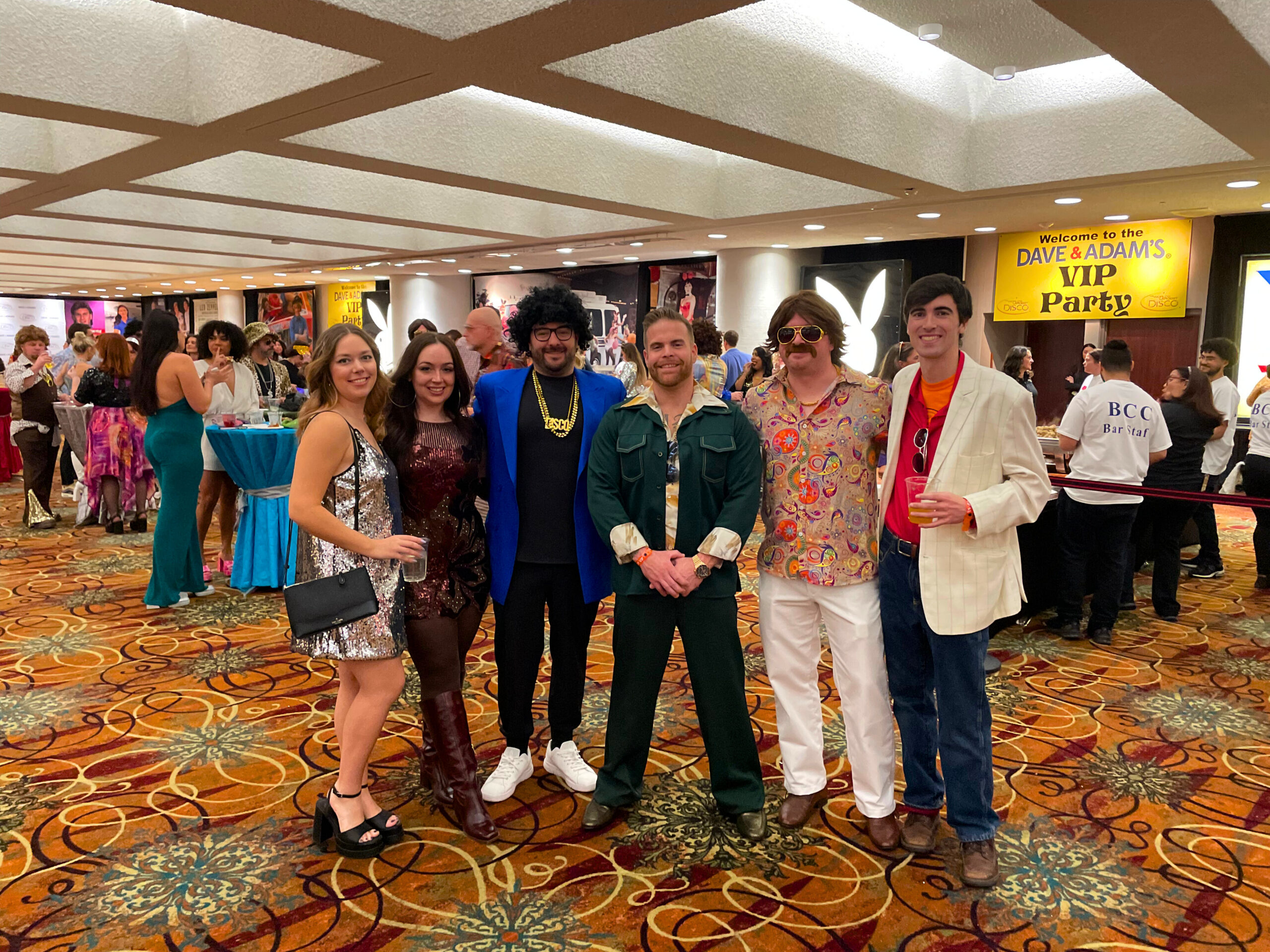 Group in retro attire at VIP party event, colorful 1970s theme.