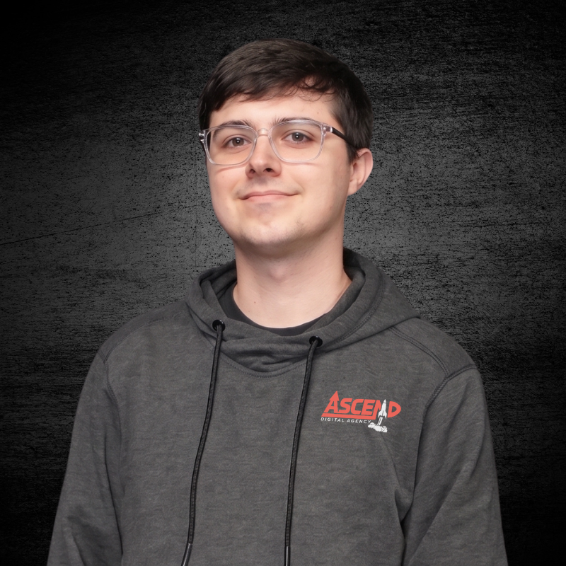Person wearing glasses and a hoodie with 'Ascend' logo, dark background.