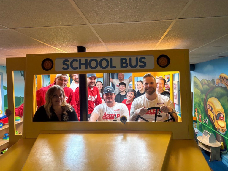 Group of smiling people inside a mock school bus at an indoor play area.