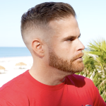 Man in red shirt by the beach with a trimmed beard and undercut hairstyle