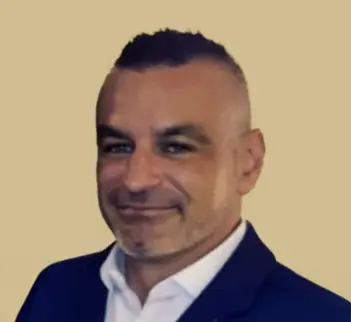 Smiling man in a navy suit against a beige background.